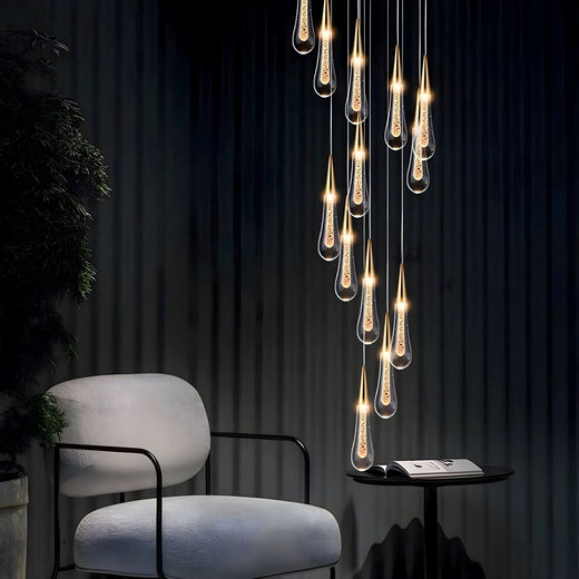 RAIN DROPS cascading warm crystal droplets beside a cream reading chair and black side table.