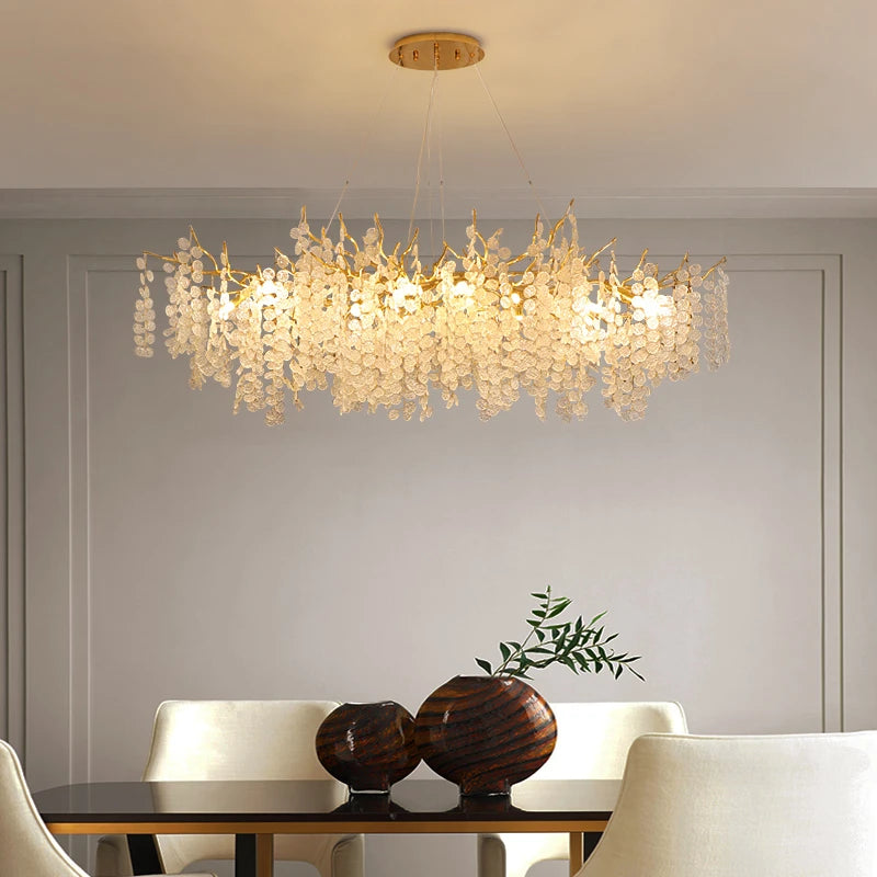 VALORA wide gold-finish branch chandelier with clear drops, lit, above a dining table
