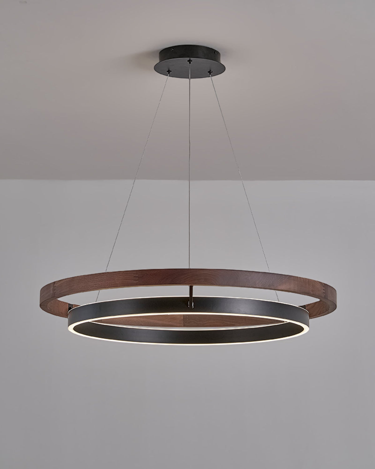 Wide walnut ORLUNEA chandelier installed low, emphasizing the glowing circular diffuser.