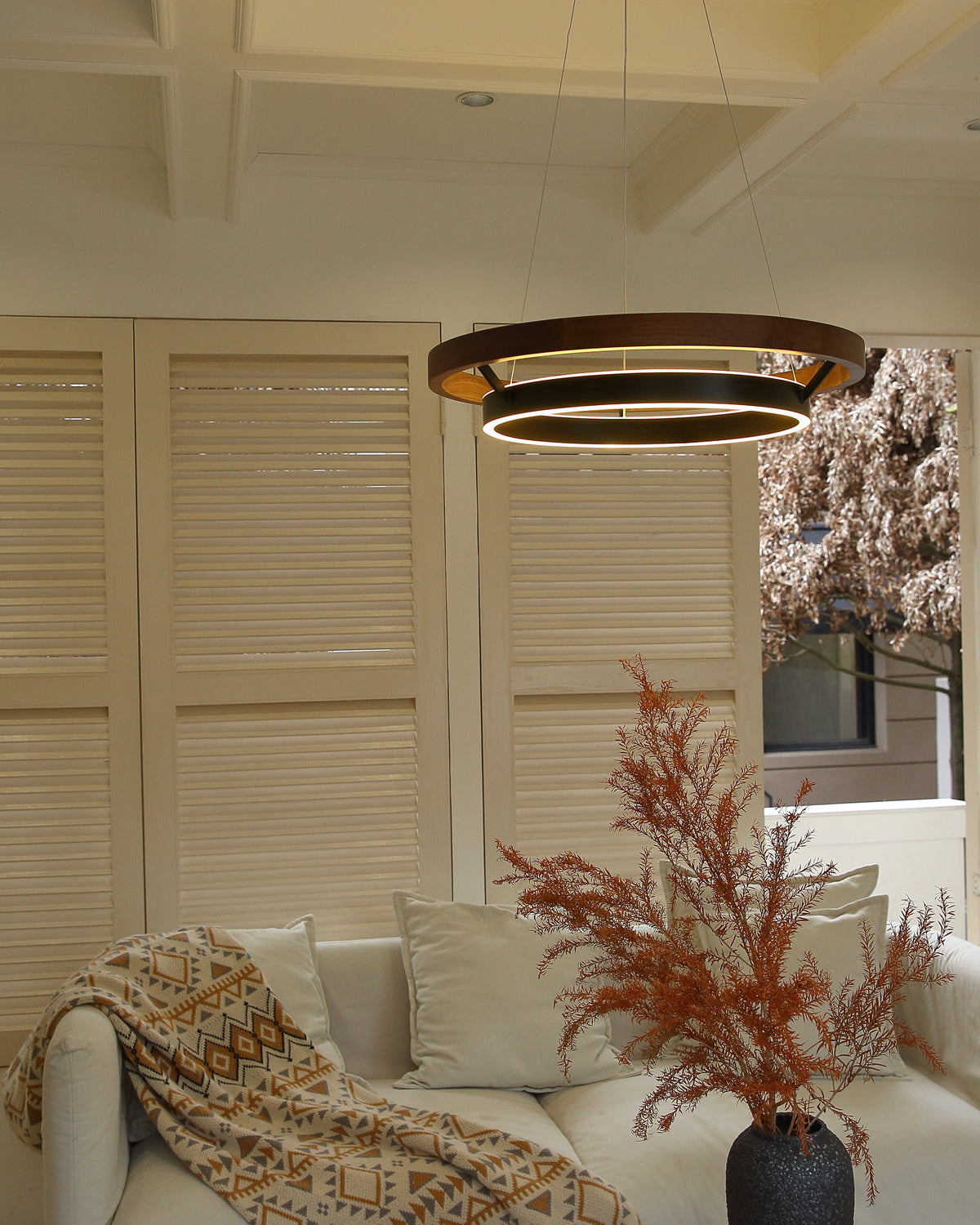Close living-room view of walnut ORLUNEA rings above a white sofa and dried foliage.