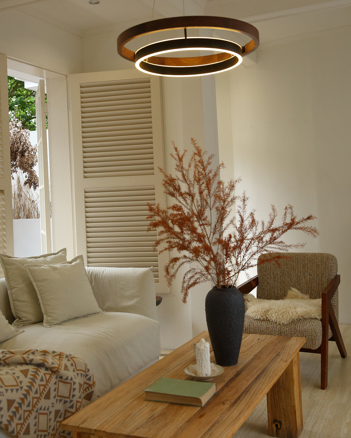 Low-angle view of glowing walnut ORLUNEA rings above a wood coffee table and armchair.