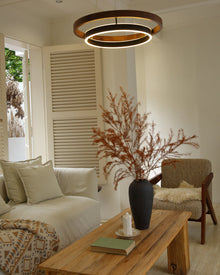 Low-angle view of glowing walnut ORLUNEA rings above a wood coffee table and armchair.