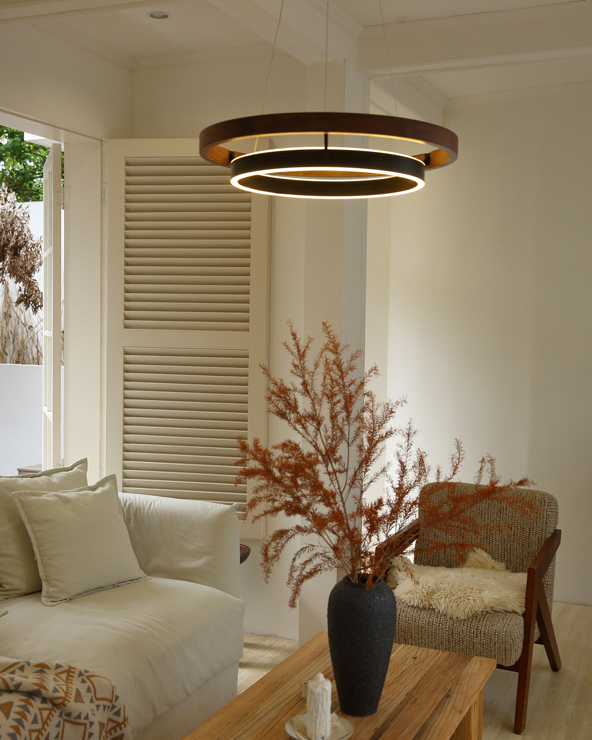 Wide walnut ORLUNEA chandelier above neutral seating in a bright shuttered room.