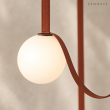CORIA close-up of stitched red-brown leather strap, flat dark globe cap and warm opal glass sphere