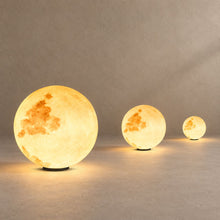 ENYA three moon-textured globe pillar lights in graduated sizes, lit, on the ground