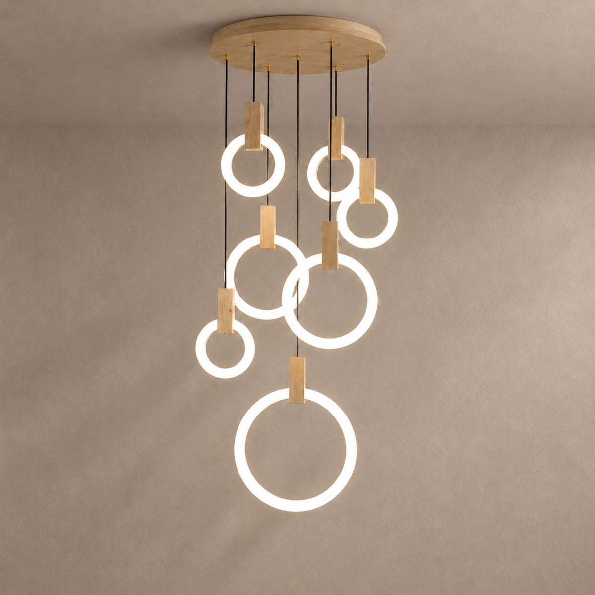 HALO seven-ring willow wood chandelier with luminous white rings on a mushroom taupe plaster background