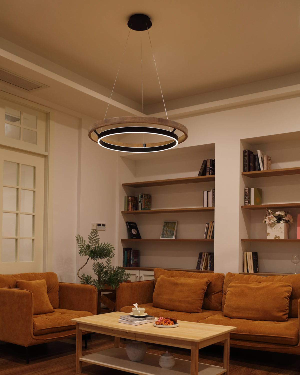 Walnut ORLUNEA ring chandelier warming a lounge with rust-colored sofas and open shelving.