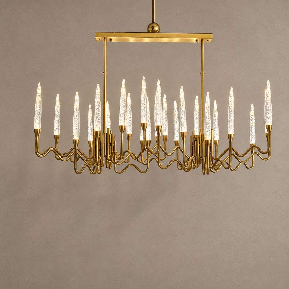 LOHA rectangular gold chandelier with clear crystal candle lights against mushroom taupe plaster