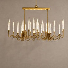 LOHA rectangular gold chandelier with clear crystal candle lights against mushroom taupe plaster