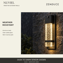 NUVIEL Dusk to Dawn Sensor in evening rain, showing weather-resistant black aluminum, clear bubble glass and warm downward light.