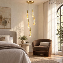 RAIN DROPS 5-light round gold chandelier above a bedside reading area with an arched window and walnut chair; photorealistic bedroom installation visualization.