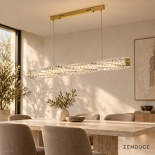 SEVRAYA gold linear chandelier with faceted twisted crystal above a pale stone dining table