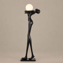 STATURO tall black figure holding a glowing white globe on a mushroom taupe background