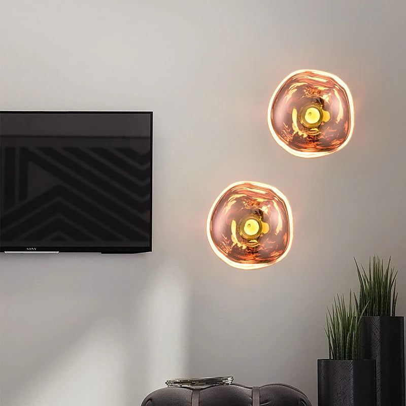 LAVA WALL pair of rose gold acrylic wall lights, lit, beside a wall-mounted TV