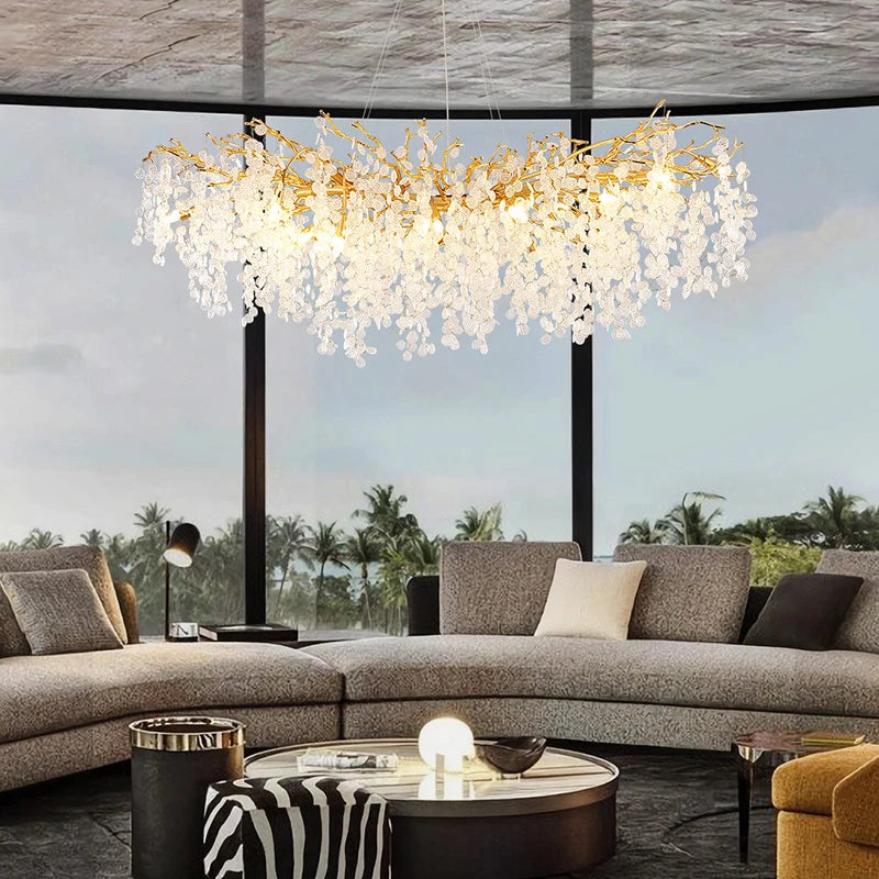 VALORA wide branch chandelier with clear drops above a curved sofa by tall windows