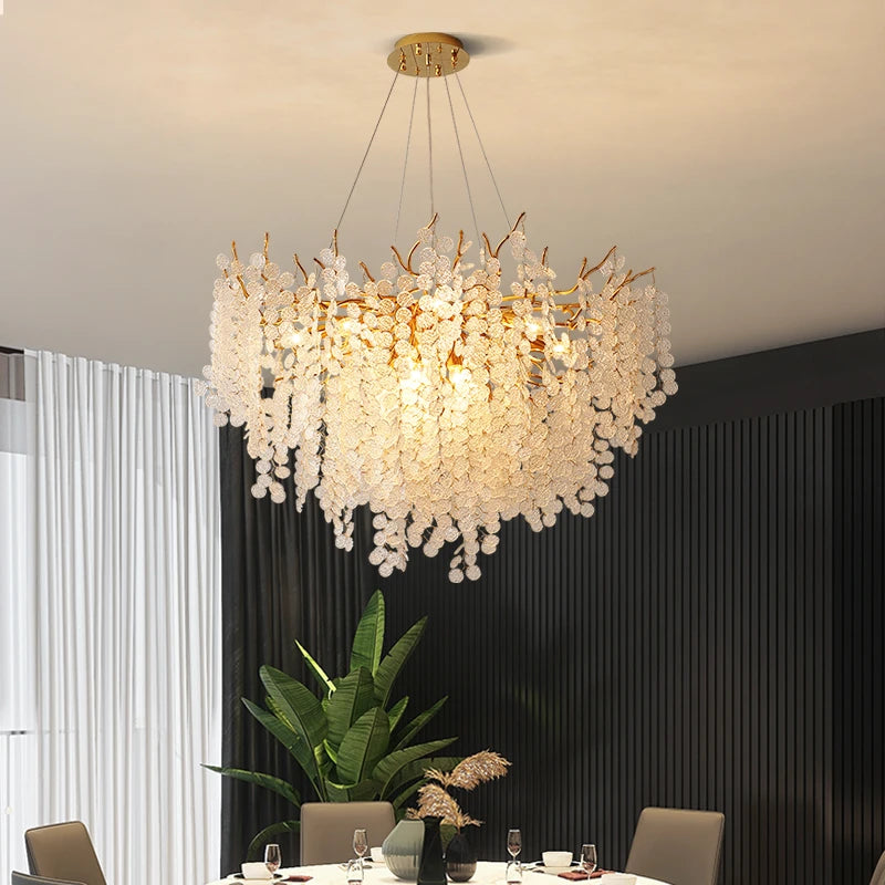 VALORA round branch chandelier with clear drops, lit, above a dining table by a curtain
