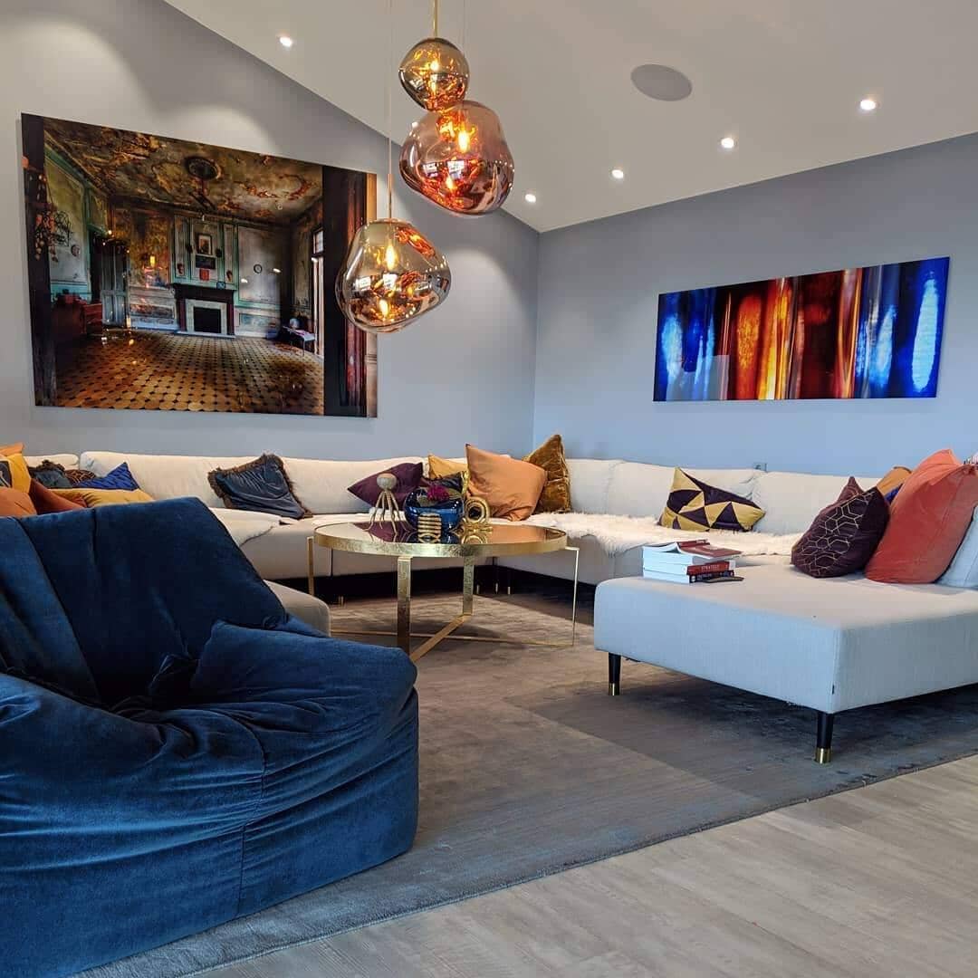 LAVA gold pendants, lit, in a living room with a blue velvet armchair and white sectional